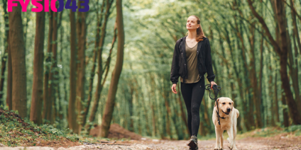 Vitamine D Jonge vrouw wandelt met haar hond in het bos om vitamine D binnen te krijgen