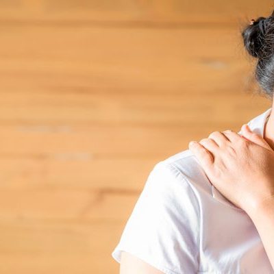 Vrouw in een wit shirt grijpt naar haar schouderklachten en schouderpijn