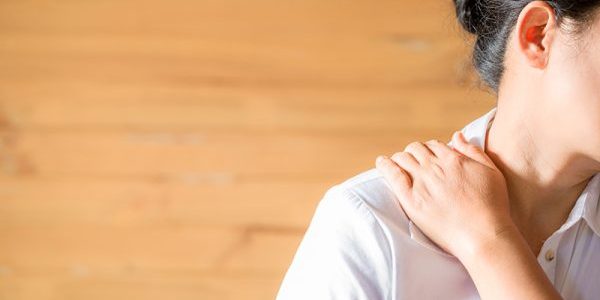 Schouderklachten Vrouw in een wit shirt grijpt naar haar schouderklachten en schouderpijn