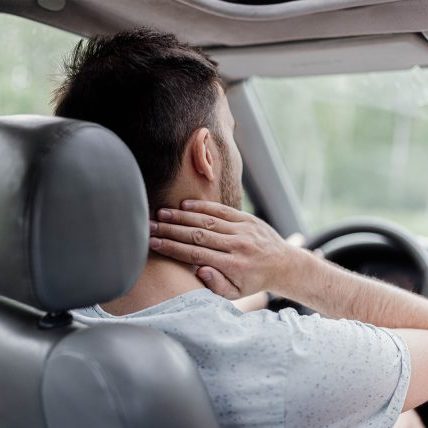 Man heeft last van nekklachten in Bunde tijdens het autorijden en voelt aan zijn nek in de auto.