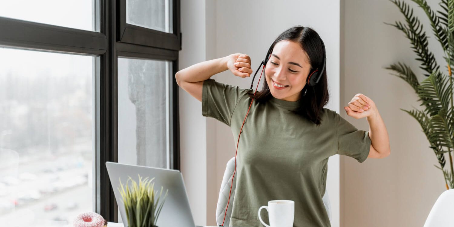 Stress en rugklachten in Maastricht Vrolijke vrouw in een groen shirt met headset op is zich aan het uitrekken en lacht terwijl ze stress en rugklachten voorkomt