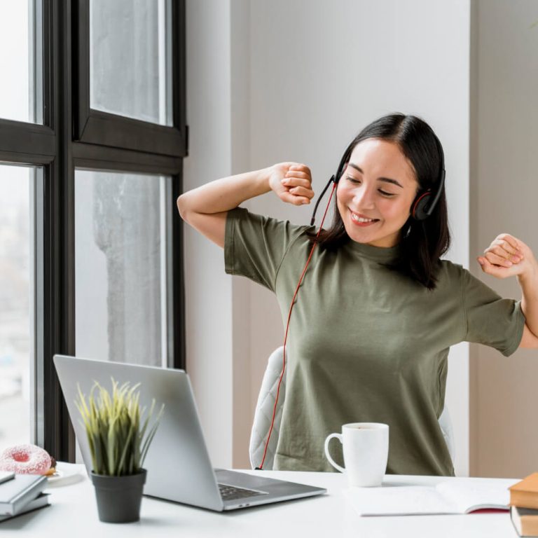 Vrolijke vrouw in een groen shirt met headset op is zich aan het uitrekken en lacht terwijl ze stress en rugklachten voorkomt