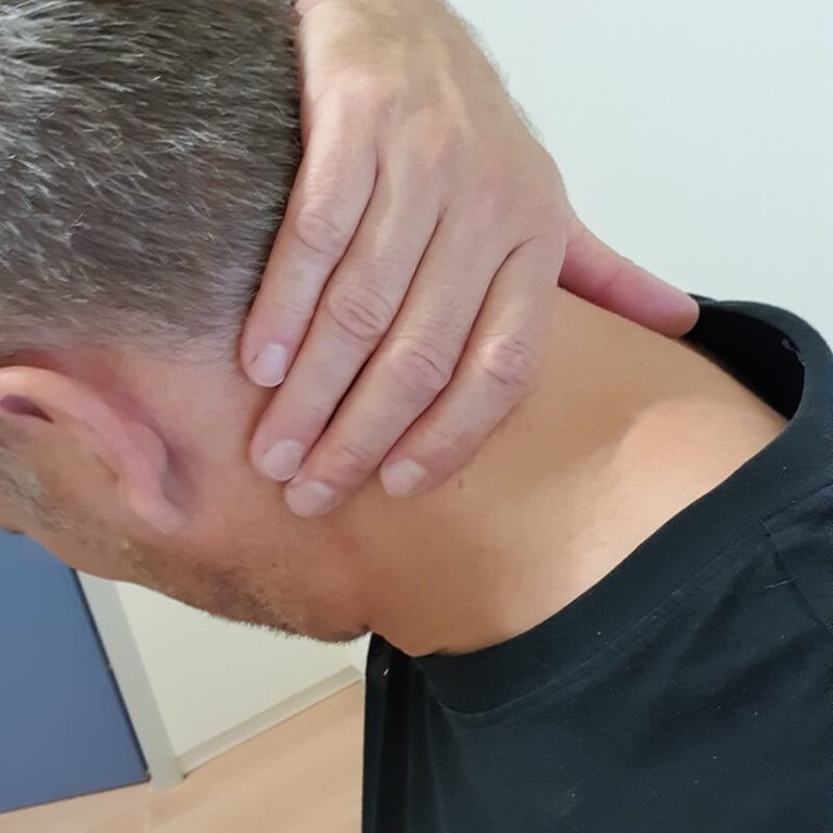 Man grijpt aan zijn nek om nekklachten en hoofdpijn te voorkomen door een opzij te kijken.