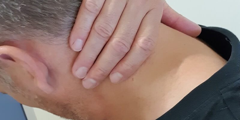 Nekklachten voorkomen Man grijpt aan zijn nek om nekklachten en hoofdpijn te voorkomen door een opzij te kijken.