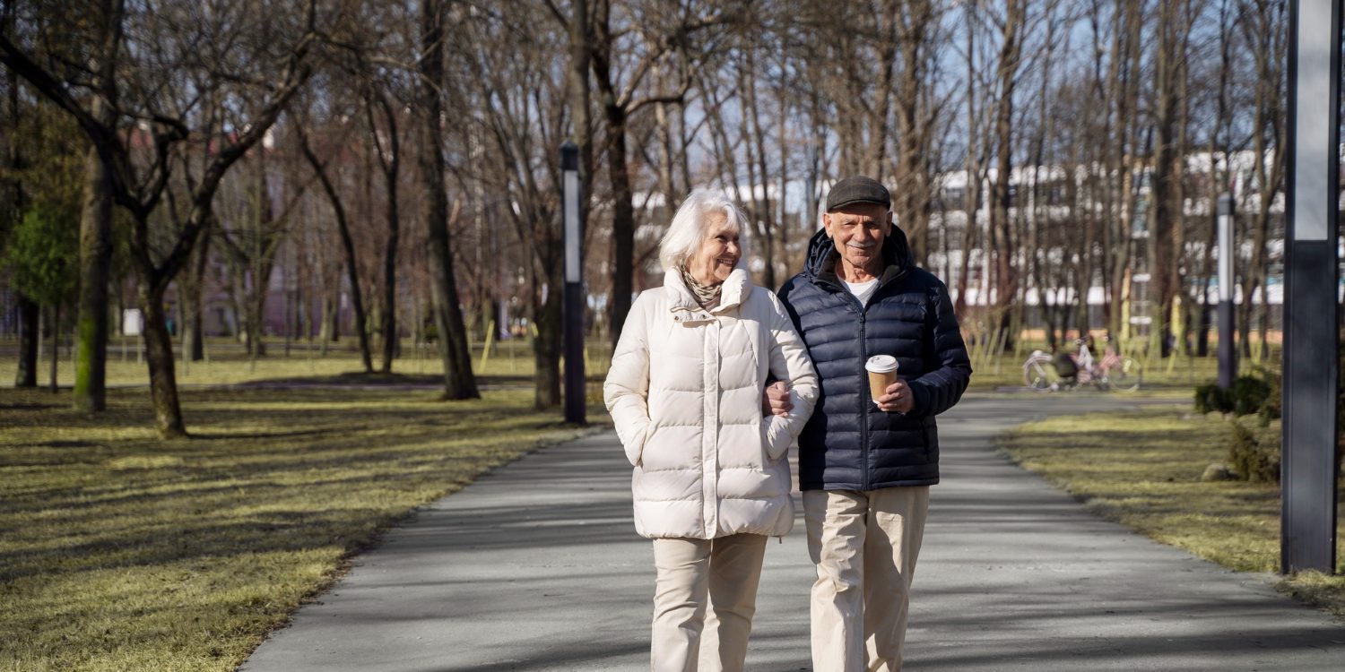 Twee ouderen zorgen voor valpreventie en maken een wandeling in het park tijdens koud weer