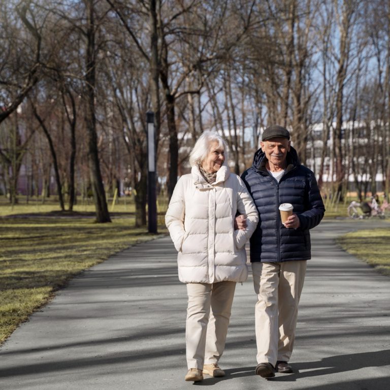 Twee ouderen zorgen voor valpreventie en maken een wandeling in het park tijdens koud weer